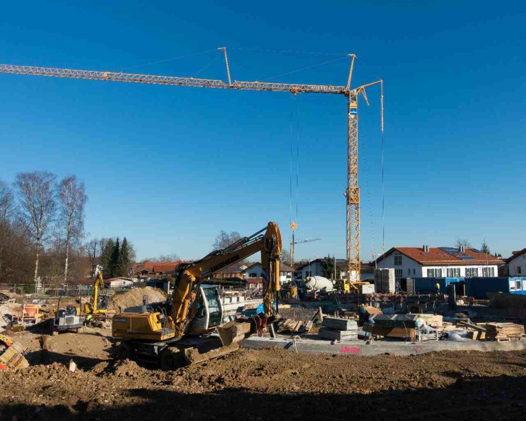 Vue d'un chantier de construction d'un lotissement avec une pelleteuse, une grue, une bétonnière, un camion toupie.